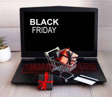Küçük bir alışveriş arabası, bir dizüstü bilgisayarın arka planında hediye ve indirimlerle doludur. Online satış kavramı.