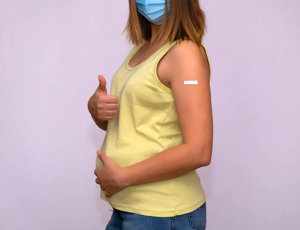 En gravid kvinna med en vaccinationstecken på axeln visar en gest av godkännande. — Stockfoto
