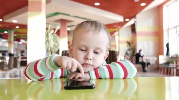 El chico en el café usa el teléfono mientras espera la orden. — Vídeos de Stock