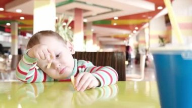 Çocuk kafede sıkılmış, patates kızartması oynuyor.