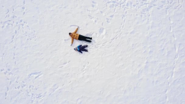 Мама і дитина роблять сніговий ангел. аерофотозйомка — стокове відео