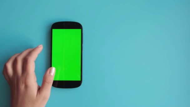 Żeńska ręka używa telefonu z zielonym ekranem na jednolitym niebieskim tle, — Wideo stockowe