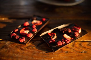 A broken chocolate bar with dried strawberries and raspberries on white background.