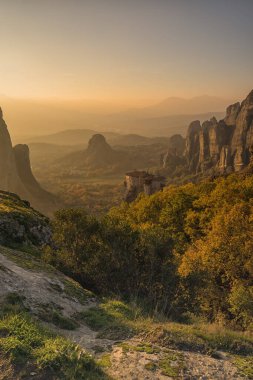 Meteora 'daki kaya oluşumları boyunca gün batımına bakarken, uzaktaki manastır Yunanistan