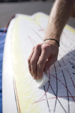 man waxing his surfboard. clipart