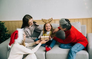 Aile Noel 'i birlikte kutlar. Büyükanne, anne ve kız kardeş küçük bir kıza hediye verir. Duygusal kız hediyeye seviniyor. Orta halli insanlar.