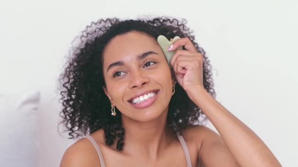 Gua Sha massaggio lifting viso con pietra di giada. Giovane donna nera massaggio viso con gua sha pietra e sorriso. routine mattutina — Video Stock