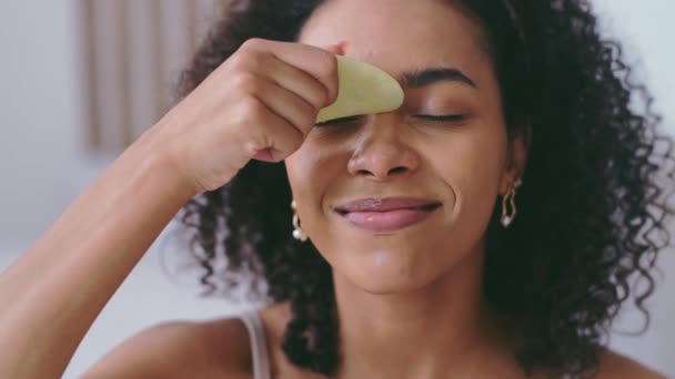 Zelfverzorging Gua Sha face lifting massage concept. Jonge Afro-Amerikaanse vrouw masseert gezicht met gua sha steen en glimlach. Ochtendroutine — Stockvideo