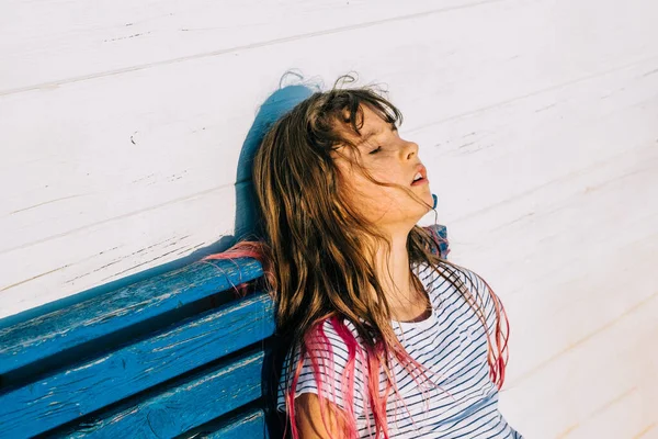 Outdoor summer portrait of cute hait colored girl suffering summer heat. The school girl sits and is exhausted from the heat after outdoor activity while hot sunny day. Jogdíjmentes Stock Képek