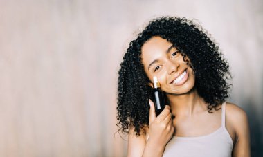 Genç melez kadın gülümsüyor ve elinde kaplıca ile kahverengi cam şişe tutuyor. Serum, terapi, cilt bakımı, sivilce önleme. Boşluğu kopyala 