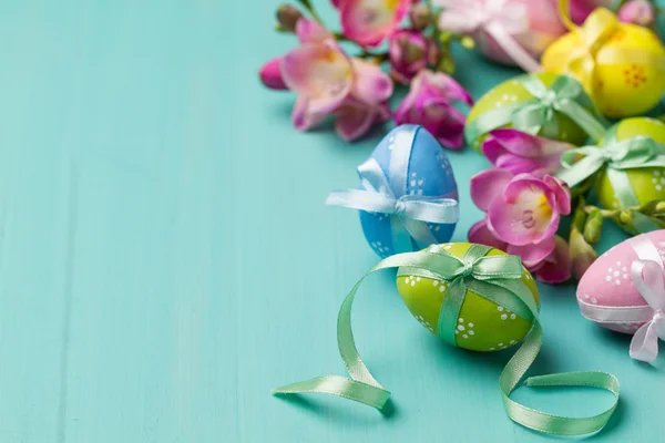 Huevos de Pascua de colores y flores en una mesa turquesa —  Fotos de Stock