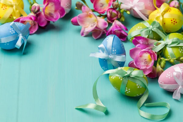 Huevos de Pascua de colores con cintas y flores en una tabla de color turquesa —  Fotos de Stock