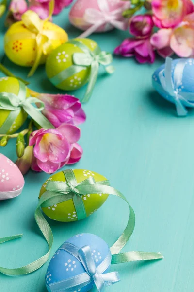 Huevos de Pascua de colores con cintas y flores en una tabla de color turquesa —  Fotos de Stock