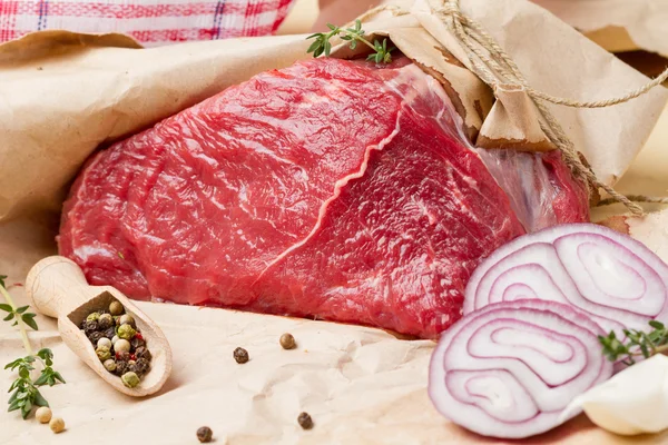 Un trozo de carne en papel de regalo, pimienta, cebolla y tomillo —  Fotos de Stock