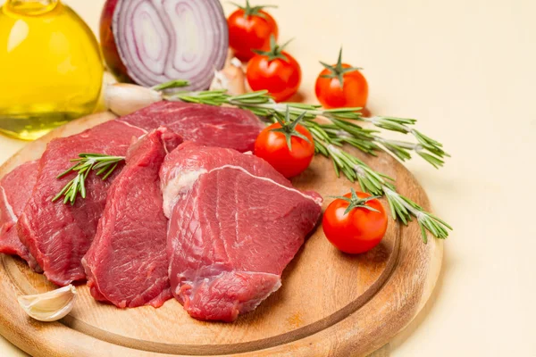 Carne sobre tabla redonda, tomates, cebollas, aceite y romero —  Fotos de Stock