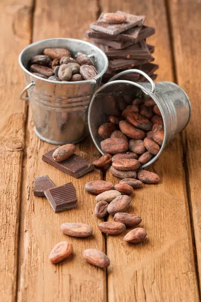 Cocoa beans in two tin buckets and dark chocolate — Stock Photo, Image