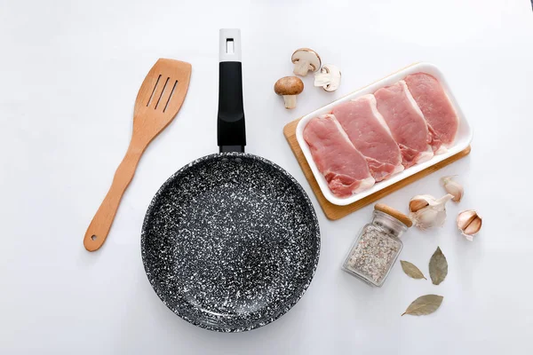 Black marble frying pan with products on light grey background, top view