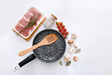 Siyah mermer kızartma tavası, çiğ et ve açık gri arka planda ahşap spatula.