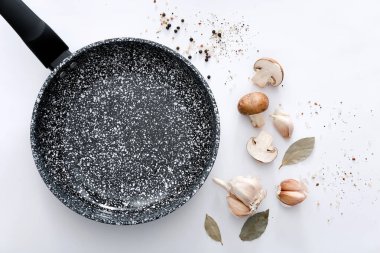 Açık gri arka planda ürünleri ve baharatları olan siyah mermer kızartma tavası.