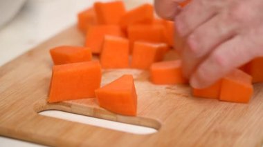 Erkek elleri pişirmek için çiğ balkabağı doğruyor, bıçakla küp küp parçalara ayırıyor.. 