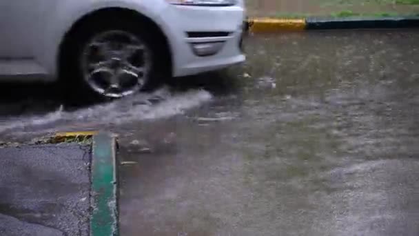 Egy fehér autó kerekei átgázolnak egy mély pocsolyán az esőben. — Stock videók