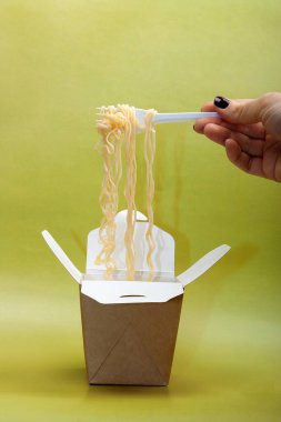 Female hand holding disposable fork with noodles over disposable paper container on green background