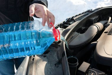 Bir adam arabanın içine cam temizleme sıvısı döker.