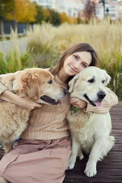 Gadis cantik memeluk dua anjing golden retriever. Outdoor — Stok Foto