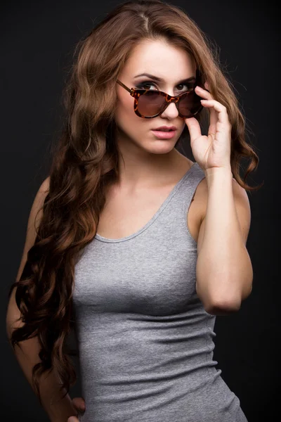 Kız gri gömlek koyu arka plan üzerinde güneş gözlüğü düzeltir