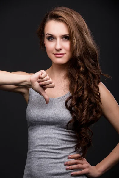 Beautiful girl in a gray shirt shows thumbs down. — Stock Photo, Image