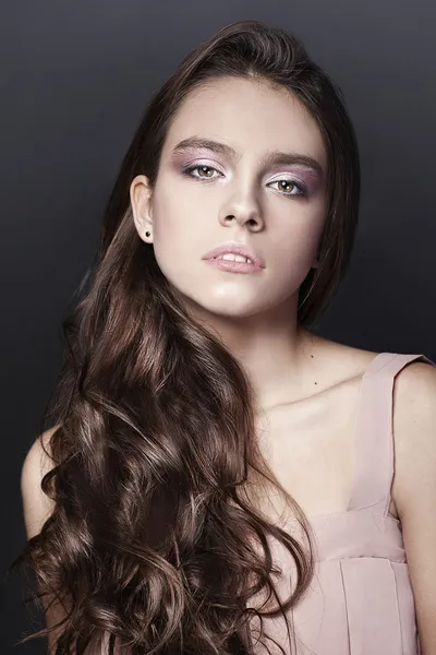 Beautiful portrait of young girl with long curly hair in pink dress on dark background — Stock Photo, Image