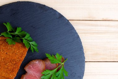 Tahta bir masada maydanozlu siyah bir tabakta doğranmış domuz carpaccio.