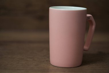 rose color mug on wooden table with green background.