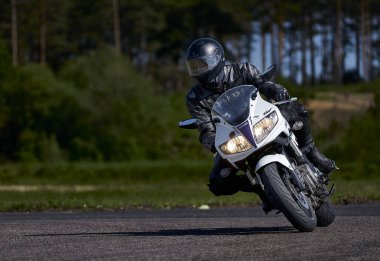 11-05-2021 Riga, Latvia Motorcyclist at sport bike rides by empty asphalt road. white sport bike. MotoGP race. Superbikes. Motorbikes racing. Motorcyclist in black suit and black helmet .