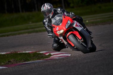 11-05-2021 Riga, Latvia Motorcyclist at sport bike rides by empty asphalt road. sport bike. MotoGP race. Superbikes. Motorbikes racing. Man in black and white suit at red sport motorcycle.