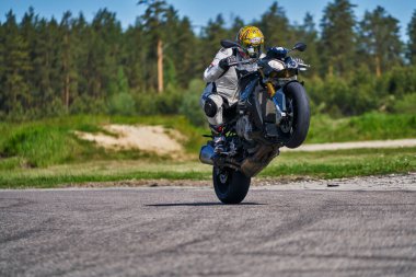 11-05-2021 Riga, Latvia Motorcyclist at sport bike rides by empty asphalt road. sport bike. MotoGP race. Superbikes. Motorbikes racing. Motorcyclist in white suit and yellow helmet making wheelie