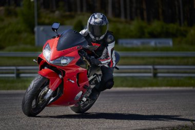 11-05-2021 Riga, Latvia Motorcyclist at sport bike rides by empty asphalt road. sport bike. MotoGP race. Superbikes. Motorbikes racing. Man in black and white suit at red sport motorcycle.