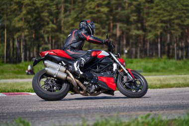 11-05-2021 Riga, Latvia Motorcyclist at sport bike rides by empty asphalt road. black red street motorcycle. MotoGP race. Superbikes. Motorbikes racing. Motorcyclist in black suit and black helmet.