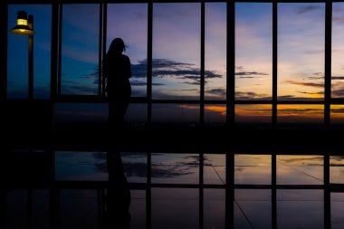 Alacakaranlık gökyüzü gün batımında pencere tarafından akıllı telefon kullanan kız