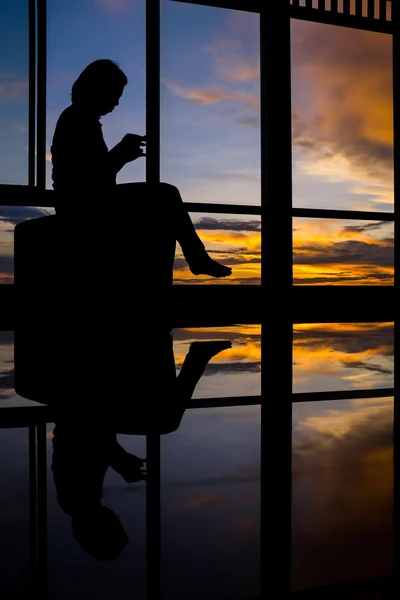 Meisje slimme telefoon door venster spelen bij zonsondergang met twilight sky — Stockfoto