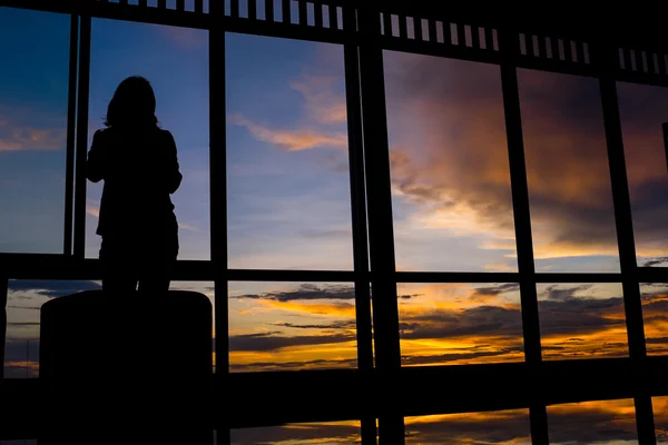 Mädchen steht bei Sonnenuntergang am Fenster mit Dämmerhimmel — Stockfoto
