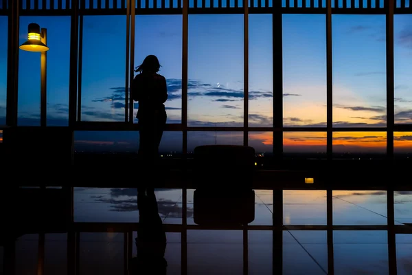 Дівчина грає смартфон за вікном на заході сонця з сутінковим небом — стокове фото