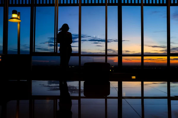 Meisje slimme telefoon door venster spelen bij zonsondergang met twilight sky — Stockfoto