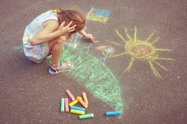 Ukrainian girl child draws children's drawings with chalk on the pavement.
