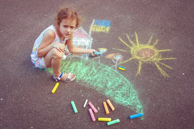Ukrainian girl child draws children's drawings with chalk on the pavement.