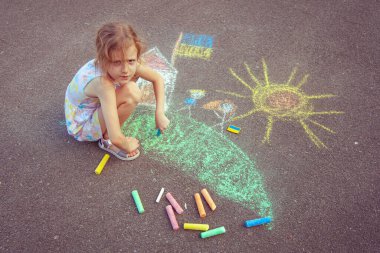Ukrainian girl child draws children's drawings with chalk on the pavement.