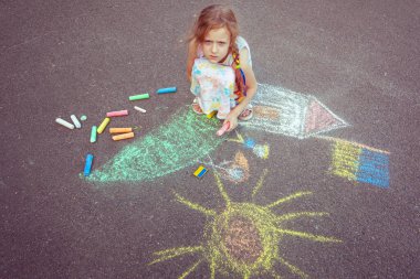 Ukrainian girl child draws children's drawings with chalk on the pavement.