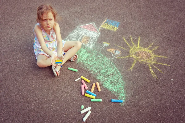 Ukrainian girl child draws children's drawings with chalk on the pavement.