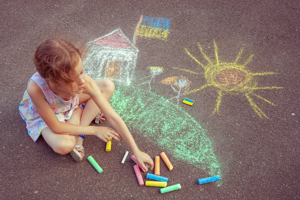 Ukrainian girl child draws children's drawings with chalk on the pavement.