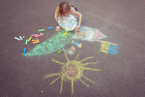Ukrainian girl child draws children's drawings with chalk on the pavement.
